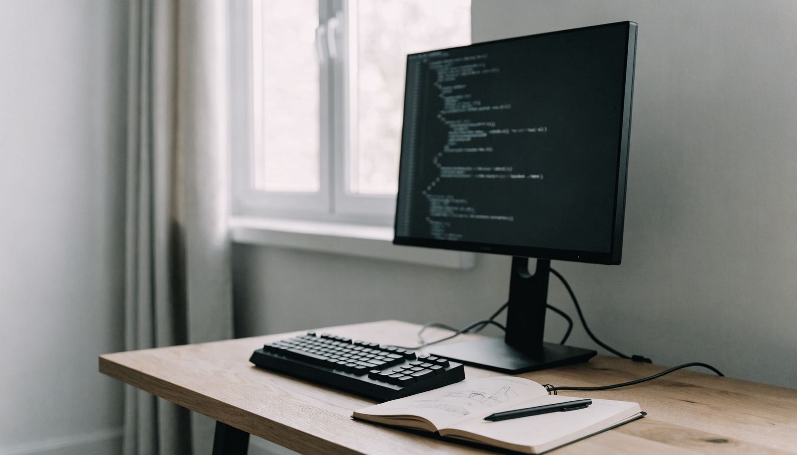 Arbeitsplatz mit Bildschirm, Tastatur und einer handgezeichneten Architekturskizze im Notizbuch